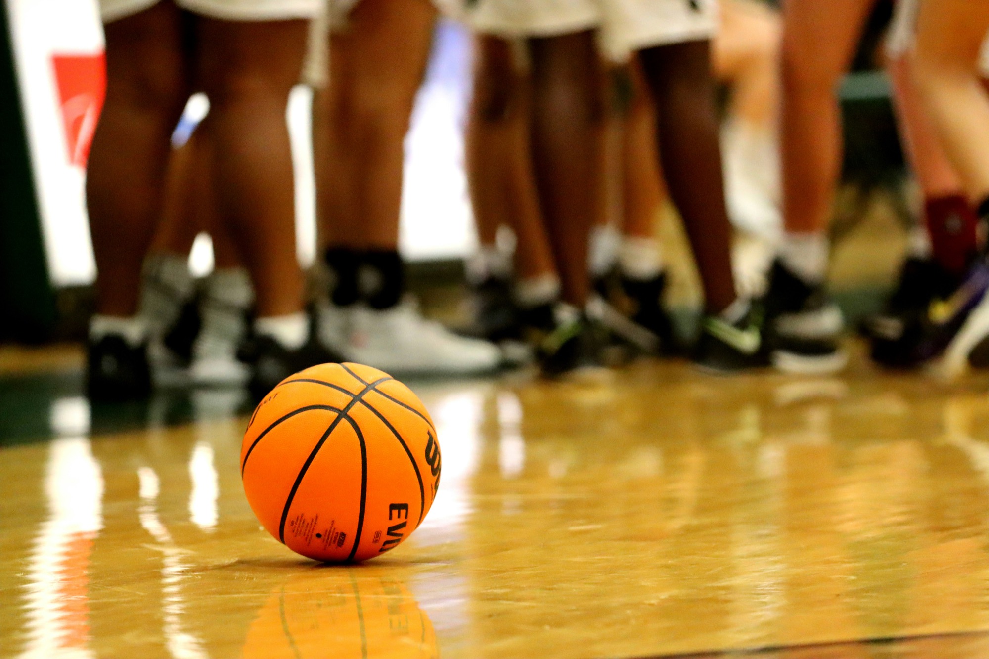 A basketball on the gym floor with a team huddled behind it
